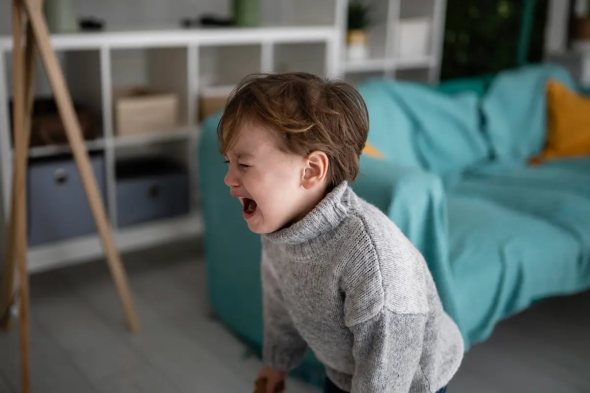 A young boy cries out and leans forward in distress at home, capturing the intensity of a child's meltdown and why emotional regulation is so hard for kids.