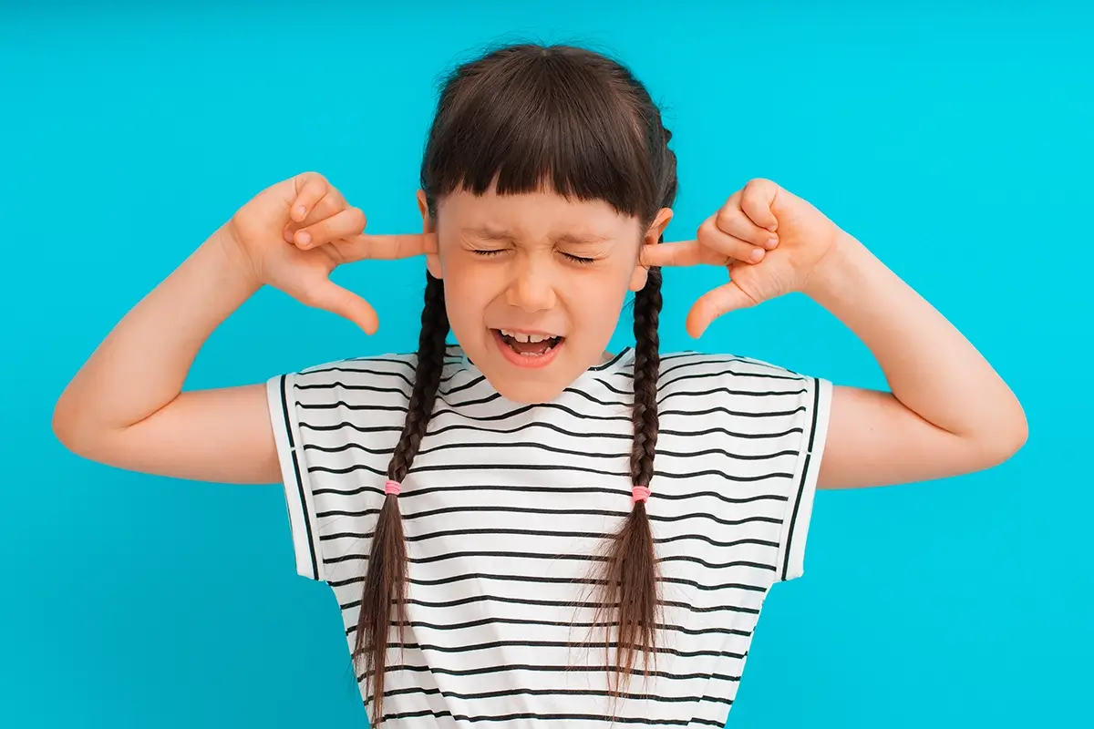 A young girl with braided pigtails plugs her fingers in her ears and squeezes her eyes shut, illustrating why kids won't listen to parents.