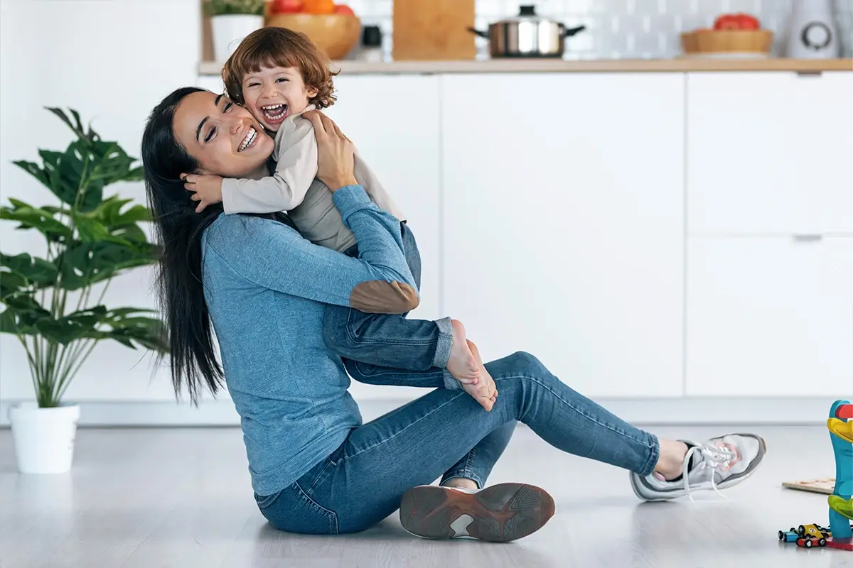 A mom holds her toddler in the air as they both laugh, demonstrating the power of co-regulation in parenting. 