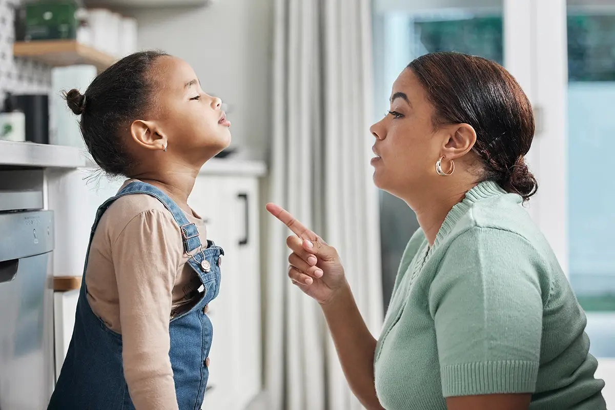 A mother points her finger while speaking firmly to her young daughter, who looks away defiantly — a familiar scene for parents wondering why their child won't listen.
